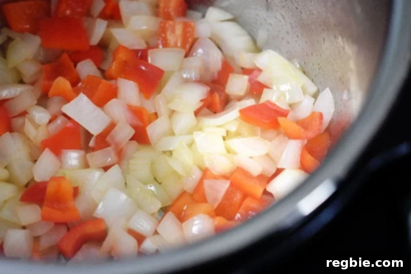 A close up of diced onions and red bell peppers being sautéed in an open Instant Pot.