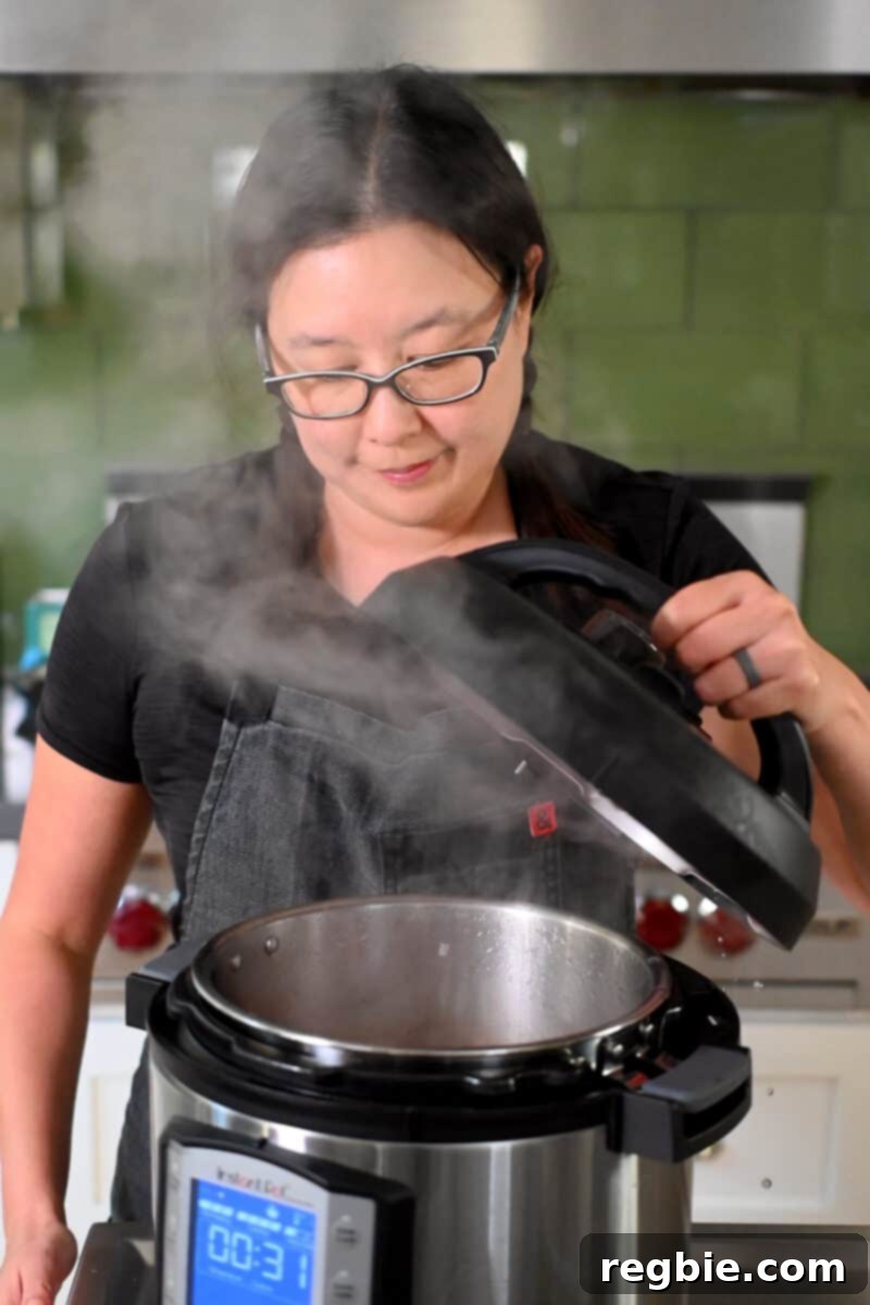 An Asian woman in glasses is opening an Instant Pot and lots of hot steam is coming out.