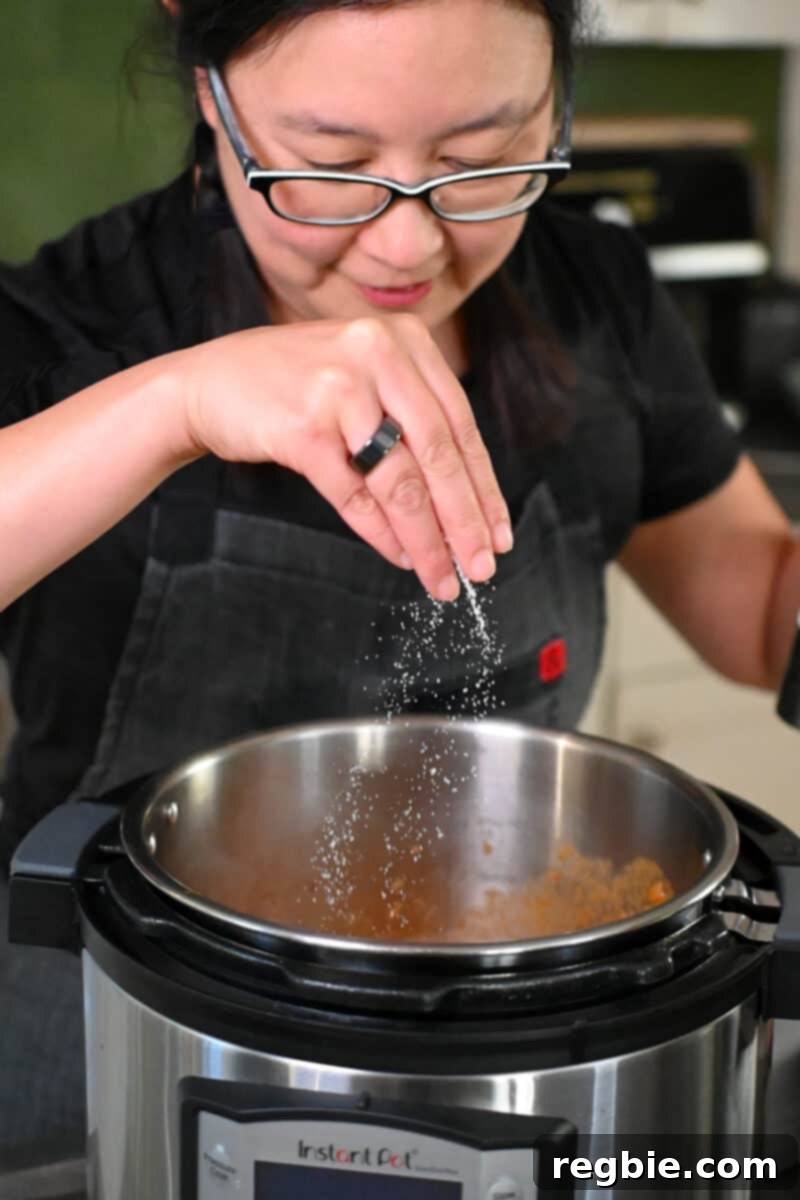 An Asian woman in glasses is seasoning the sauce for lamb shanks in an Instant Pot.