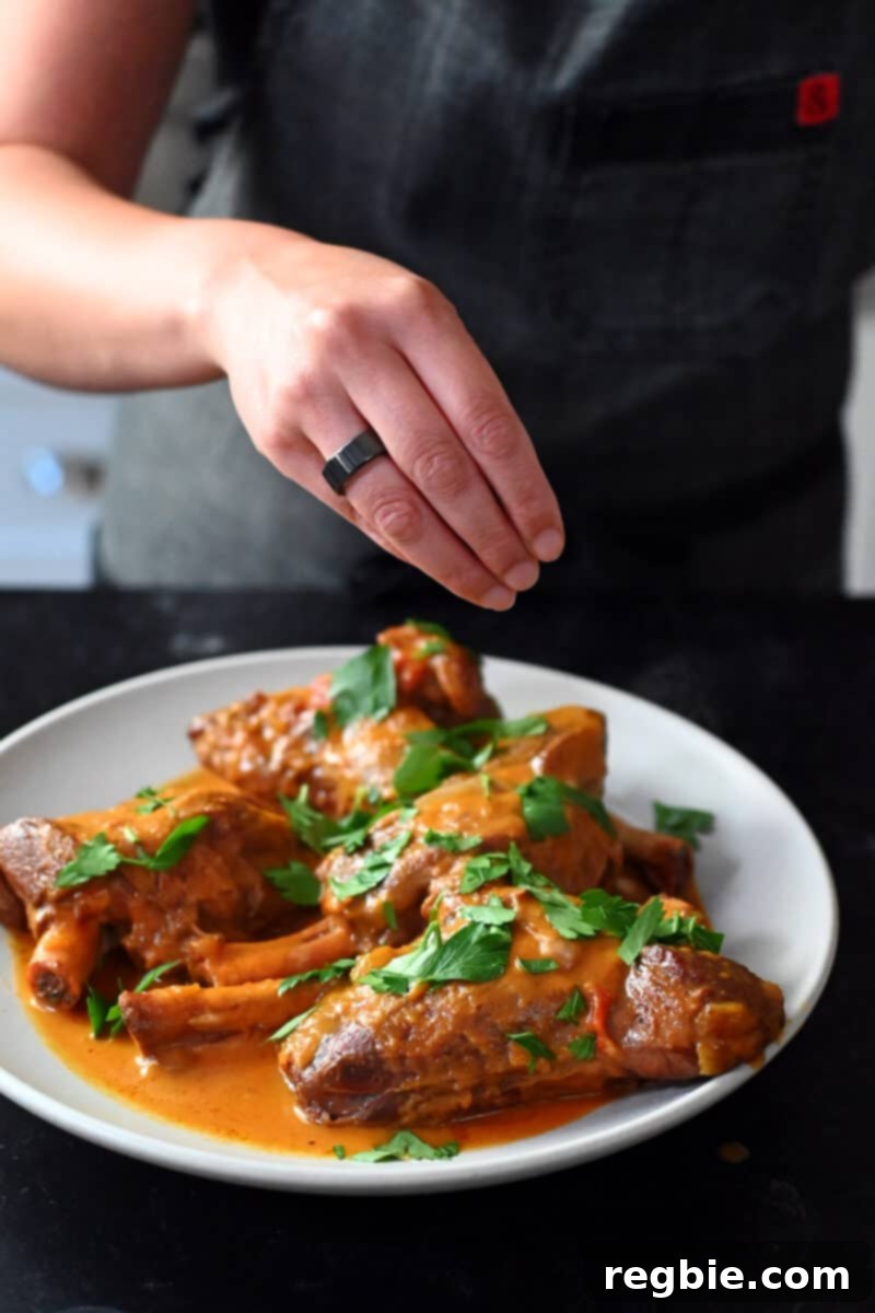 A hand is sprinkling fresh Italian parsley on some lamb shanks cooked in an Instant Pot.
