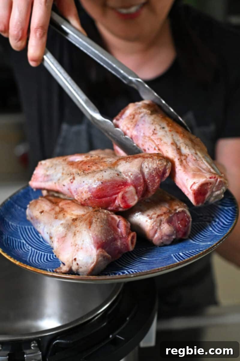 Using tongs to transfer seared lamb shanks from an Instant Pot onto a platter.