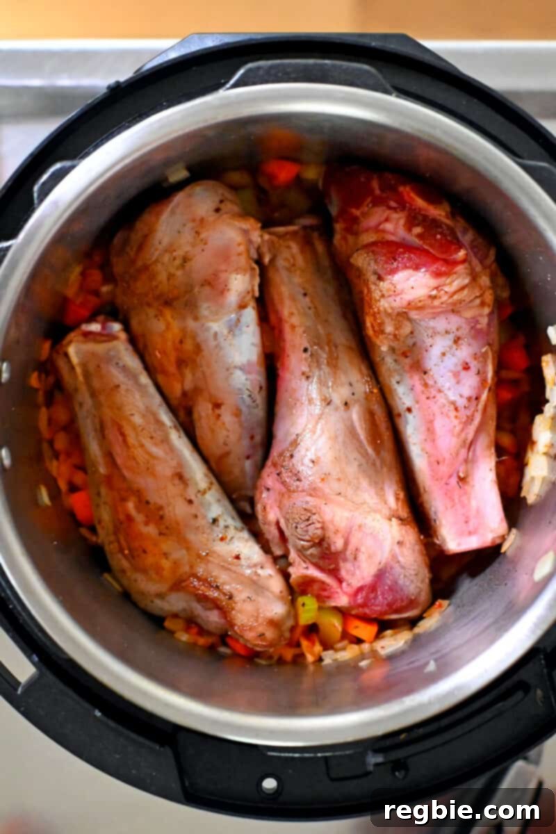 An overhead shot of an open Instant Pot with four seared lamb shanks on top of diced vegetables.