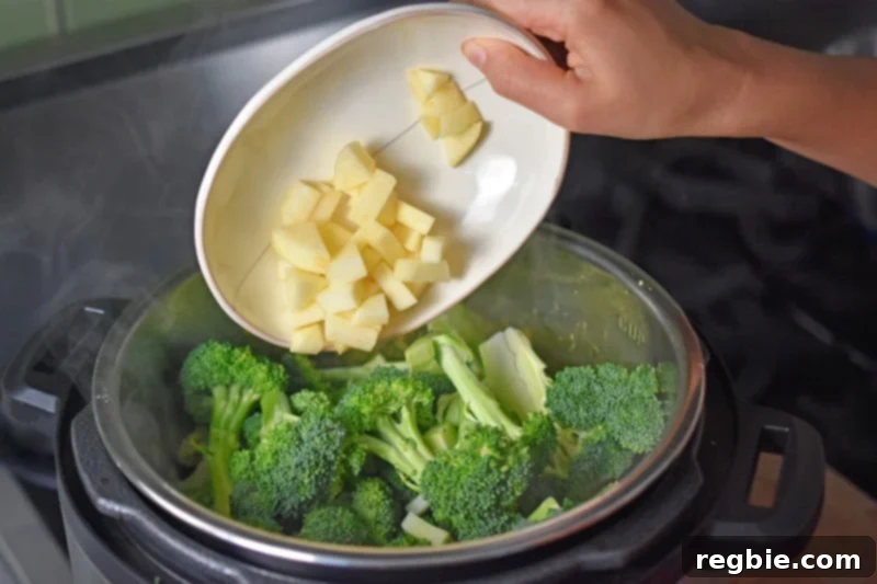 Diced apple being added to the Instant Pot with broccoli and other ingredients for Curried Cream of Broccoli Soup, showcasing the 'secret ingredient' for balanced sweetness.
