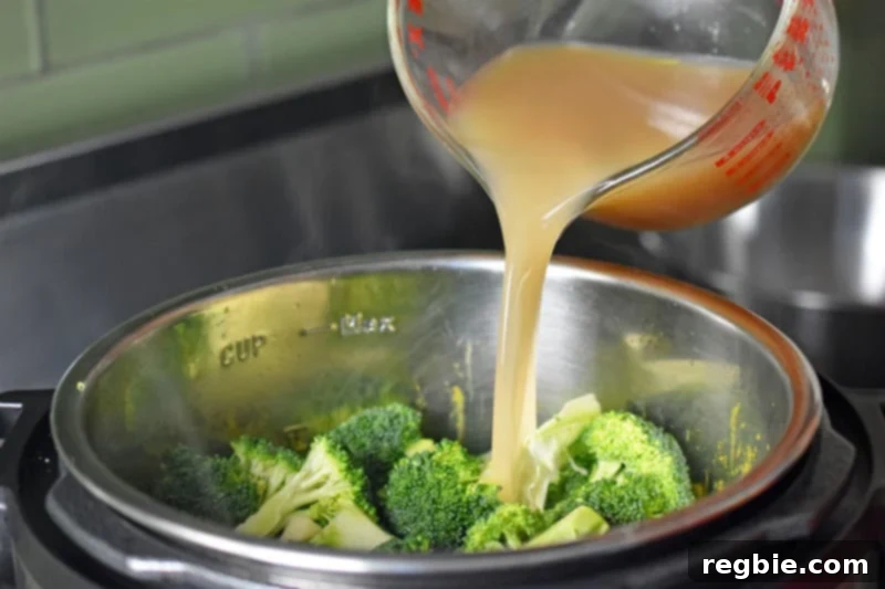 A steady stream of broth being poured into the Instant Pot, covering the vegetables to cook the Curried Cream of Broccoli Soup under pressure.