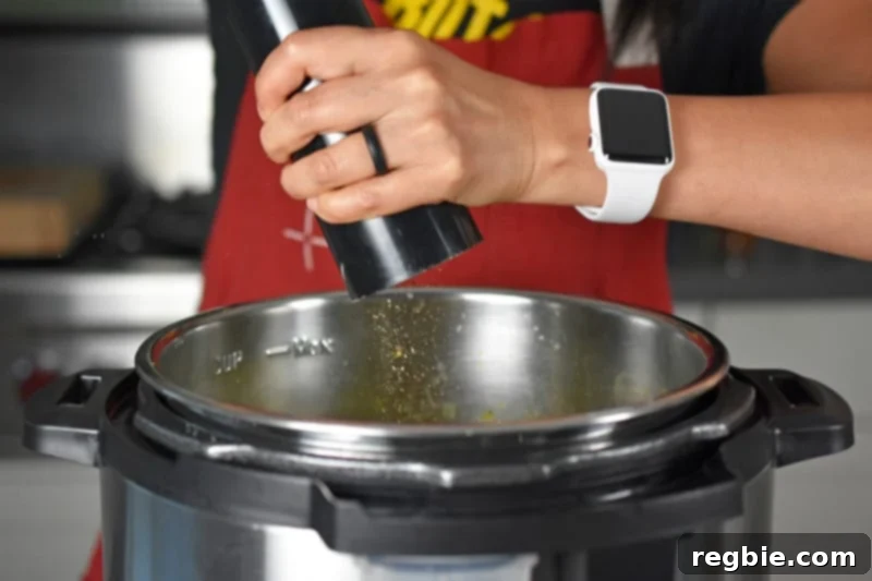 A hand grinding fresh black pepper into a pot of Instant Pot Curried Cream of Broccoli Soup, enhancing its flavor before serving.