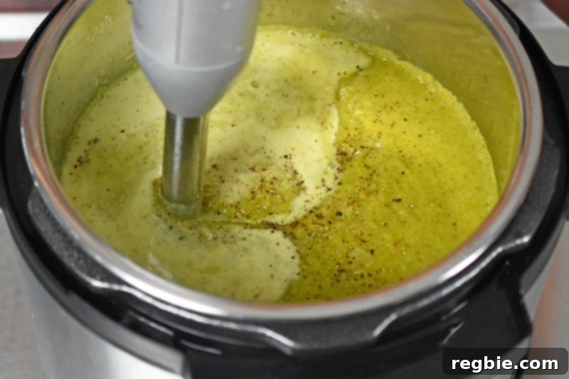 An immersion blender mixing in coconut milk to the Instant Pot Curried Cream of Broccoli Soup, ensuring a perfectly smooth and creamy dairy-free texture.