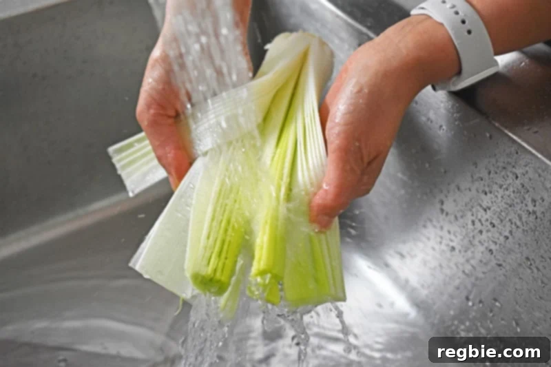 A close-up of someone meticulously rinsing sliced leeks under running water, ensuring all dirt is removed for the Instant Pot Curried Cream of Broccoli Soup.