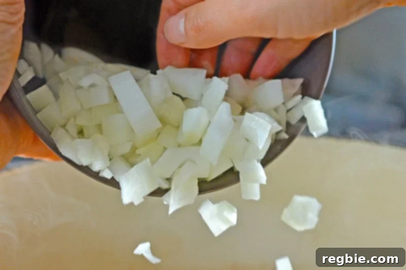 Chopped onions being added to a hot Instant Pot, a suitable substitute for leeks and shallots in this paleo Curried Cream of Broccoli Soup recipe.