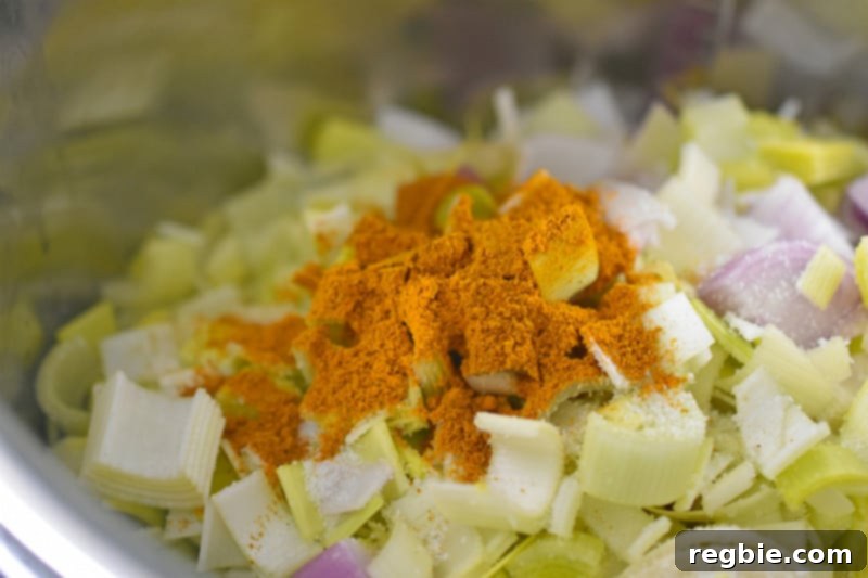 A close-up shot inside the Instant Pot showing chopped vegetables being seasoned with Indian curry powder and a sprinkle of salt, creating an aromatic foundation for the dairy-free soup.
