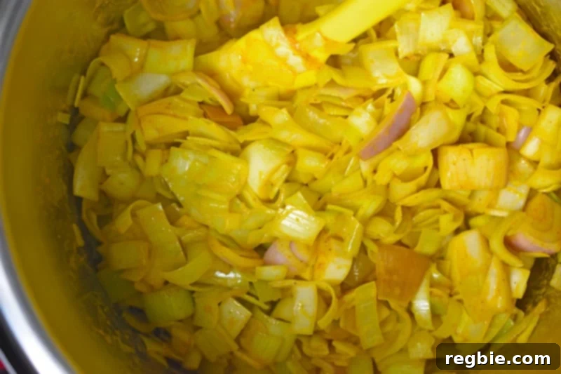 An overhead view of sautéed leeks, shallots, and curry powder inside an Instant Pot, beautifully fragrant and softened, ready for the next ingredients.