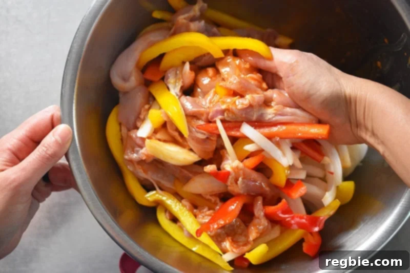 Using hands to thoroughly toss and combine chicken and vegetables with the marinade for Sheet Pan Chicken Fajitas.