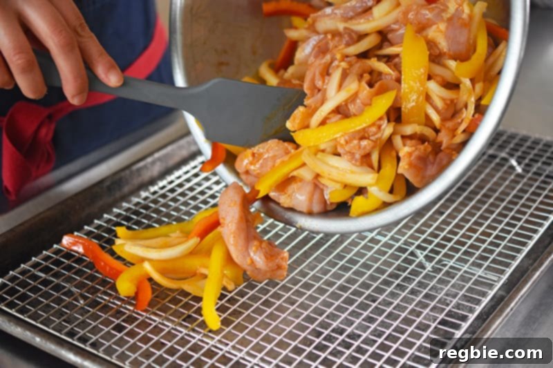 Placing the marinated chicken fajitas and vegetables evenly onto the wire rack on the rimmed baking sheet.