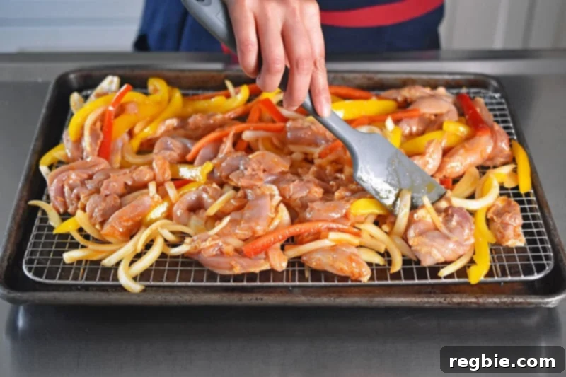 Using a silicone spatula to spread the Sheet Pan Chicken Fajitas ingredients in a single layer on the wire rack for even cooking.