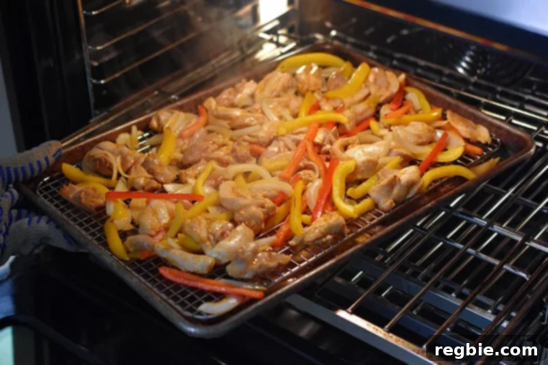 Turning the Sheet Pan Chicken Fajitas 180° at the halfway point of the baking process to ensure even cooking and browning.