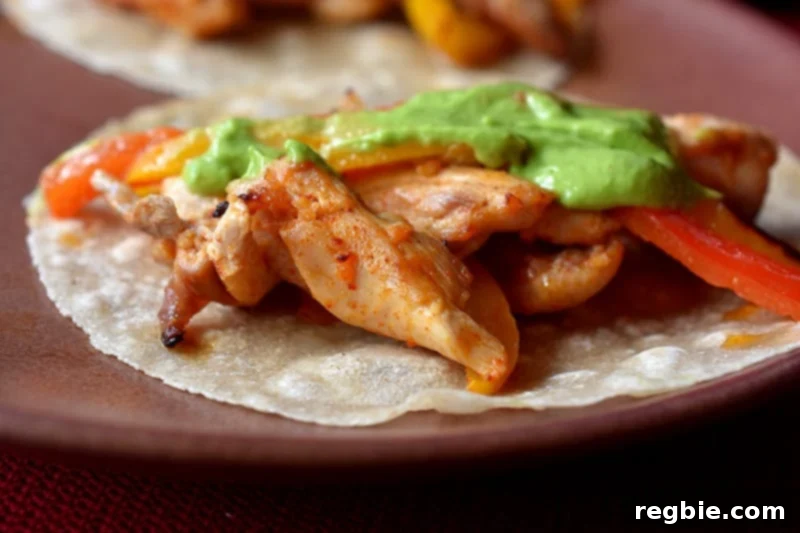 A closeup of a grain-free tortilla topped with Sheet Pan Chicken Fajitas and dairy-free Avocado Crema.