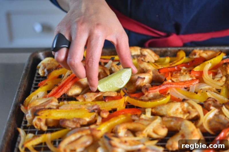 Placing fresh sliced limes on a finished tray of Sheet Pan Chicken Fajitas, ready for serving.