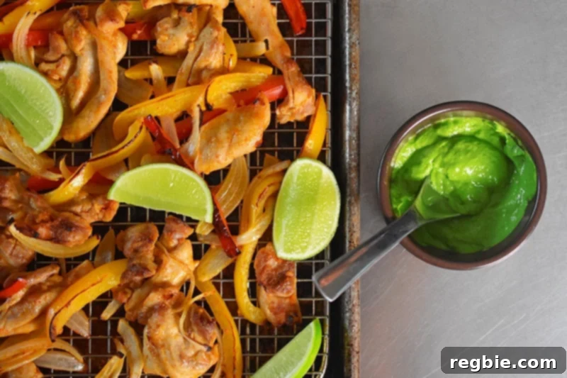 Overhead shot of crispy Sheet Pan Chicken Fajitas alongside a bowl filled with fresh, dairy-free Avocado Crema.