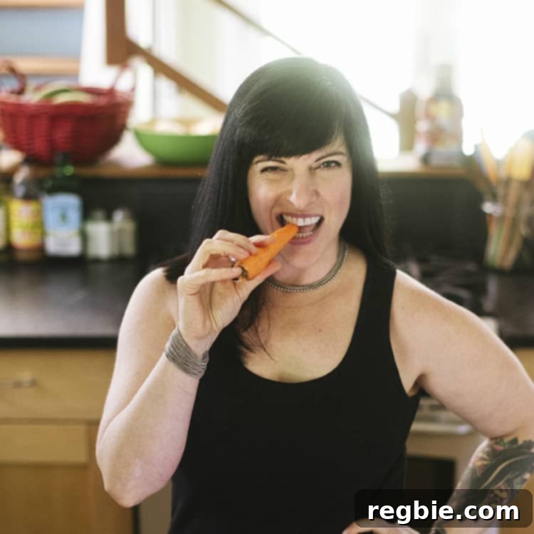 Keto Whole30 Spicy Dan Dan Noodles 2 Picture of Melissa Joulwan, the author of Well Fed Weeknights, eating a carrot in her kitchen, smiling happily.
