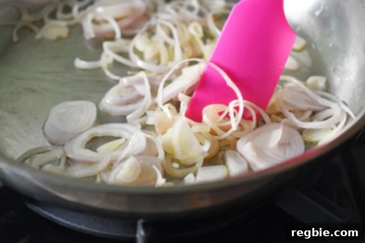 Golden-Crisp Cantonese Chicken Thighs 5 Stirring sliced shallots in a frying pan with a silicone spatula