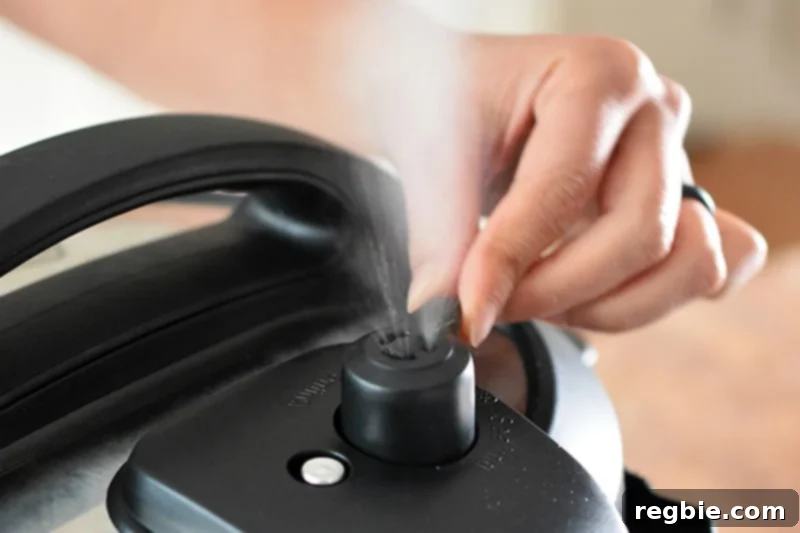 A hand is manually releasing the pressure on an Instant Pot, showing steam escaping.