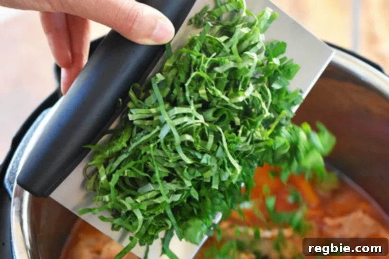 A hand is adding minced fresh herbs to the Instant Pot Summer Italian Chicken stew.