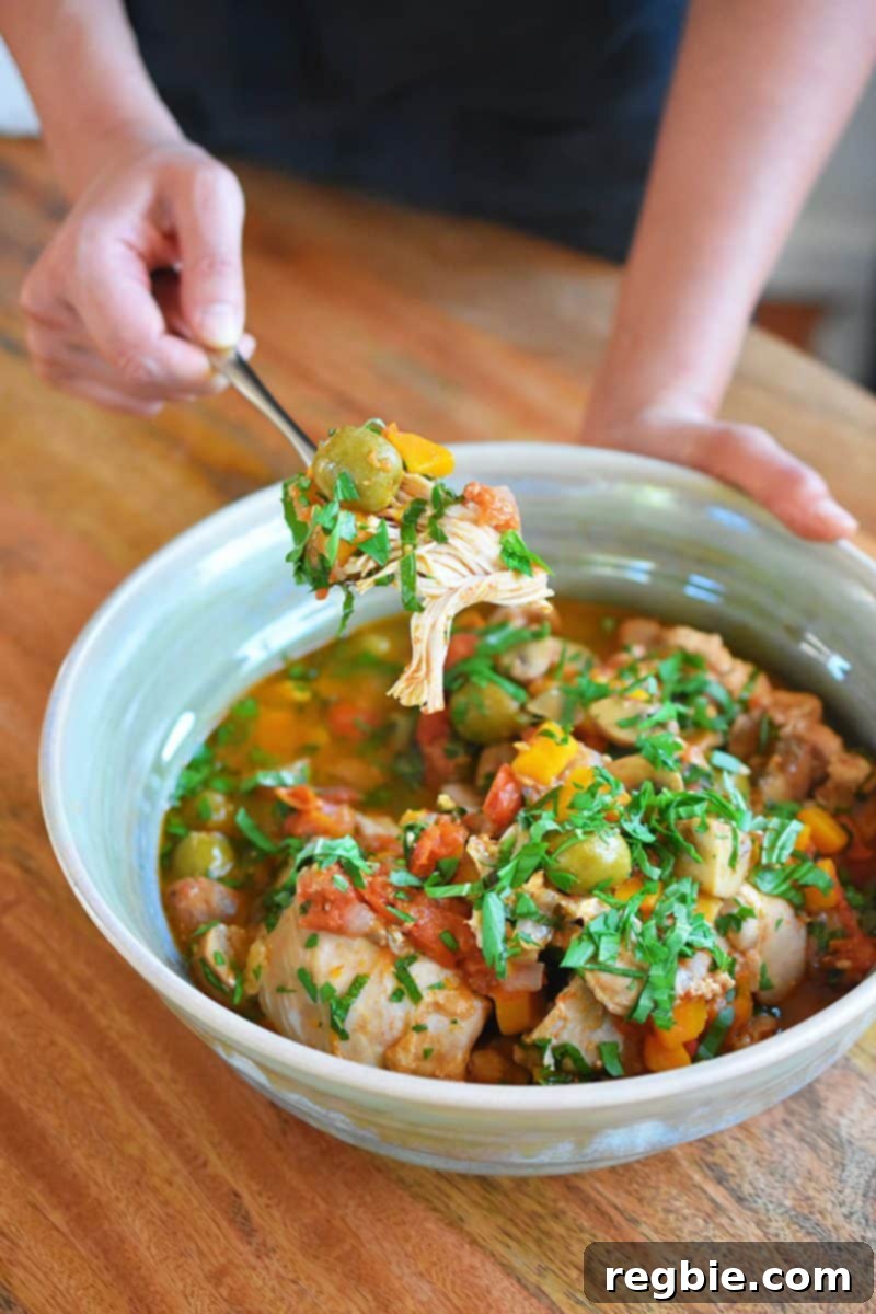 A hand is spooning Whole30, keto, Paleo Instant Pot Summer Italian Chicken out of a serving bowl, ready to be eaten.
