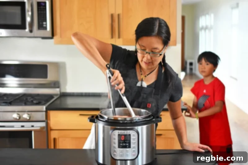 An Asian woman is using tongs to stir Instant Pot Summer Italian Chicken while a small boy watches, illustrating easy family cooking.