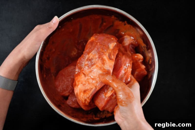 A hand mixing the Paleo Char Siu marinade thoroughly with the pork shoulder pieces in a bowl.