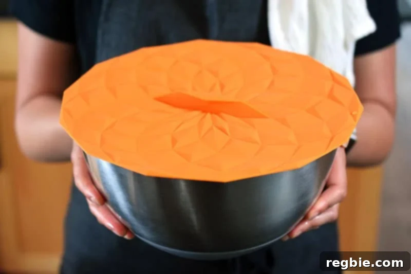 A large silver mixing bowl, covered securely with a silicone lid, containing the marinated pork for Paleo Char Siu.
