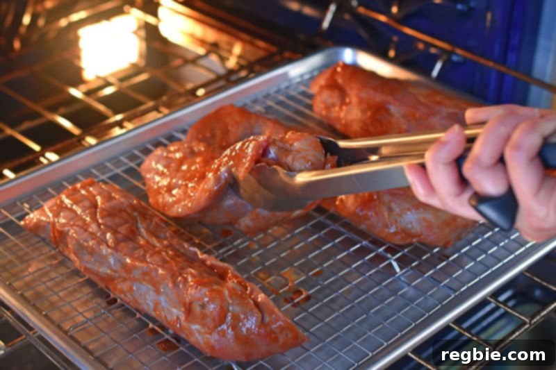 A pair of tongs flipping Paleo Char Siu pork pieces on a wire rack as they bake in the oven during the first roasting phase.