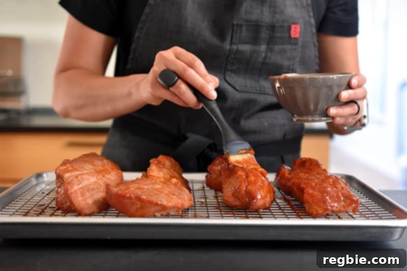 Brushing the rich, reserved marinade onto the partially roasted Paleo Char Siu (Chinese BBQ Pork) pieces.