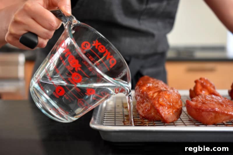 Pouring water into the rimmed baking sheet beneath the wire rack holding Paleo Char Siu (Chinese BBQ Pork) to prevent burning.