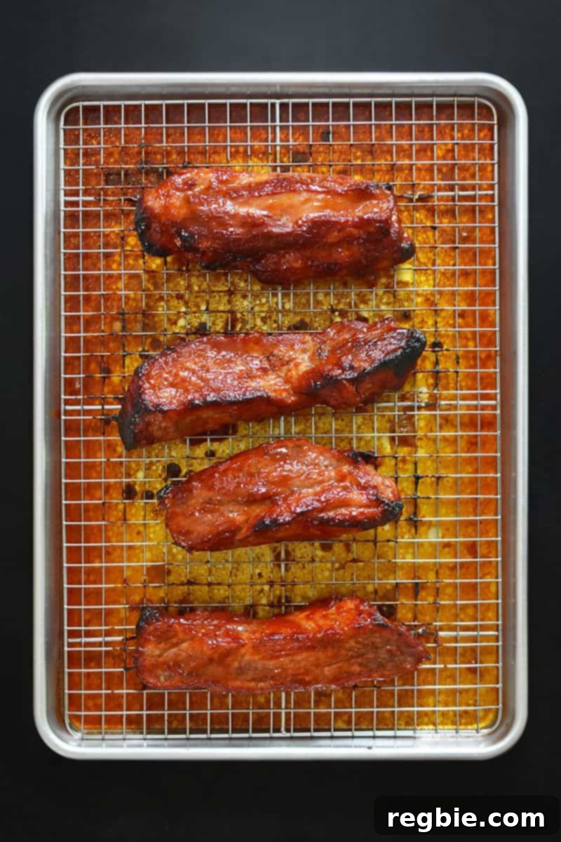 An overhead shot of perfectly roasted Paleo Char Siu (Chinese BBQ Pork) on a rimmed baking sheet and wire rack, fresh out of the oven, with beautifully charred edges.