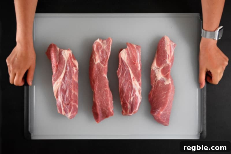 Four evenly sliced pieces of boneless pork shoulder, prepared for marination, resting on a wooden cutting board.