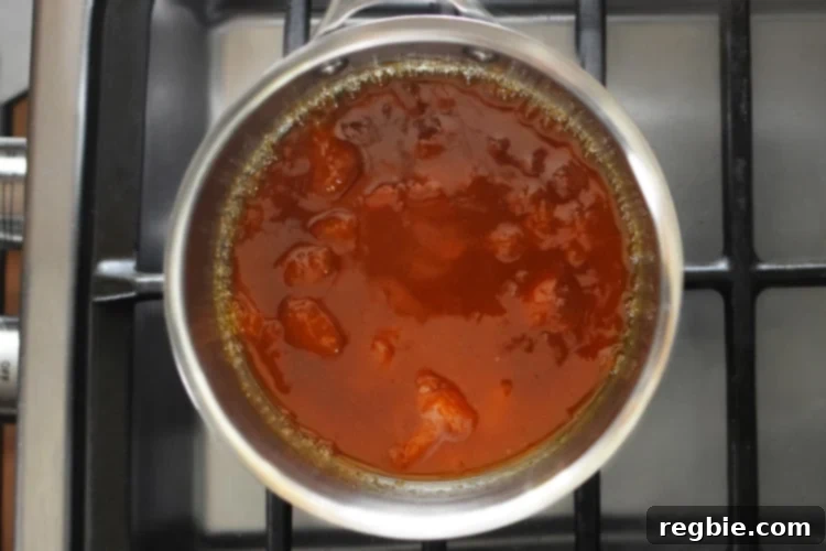 An overhead shot of a small saucepan filled with simmering Apricot-Ginger Sauce for Paleo Curry Turkey Bites.