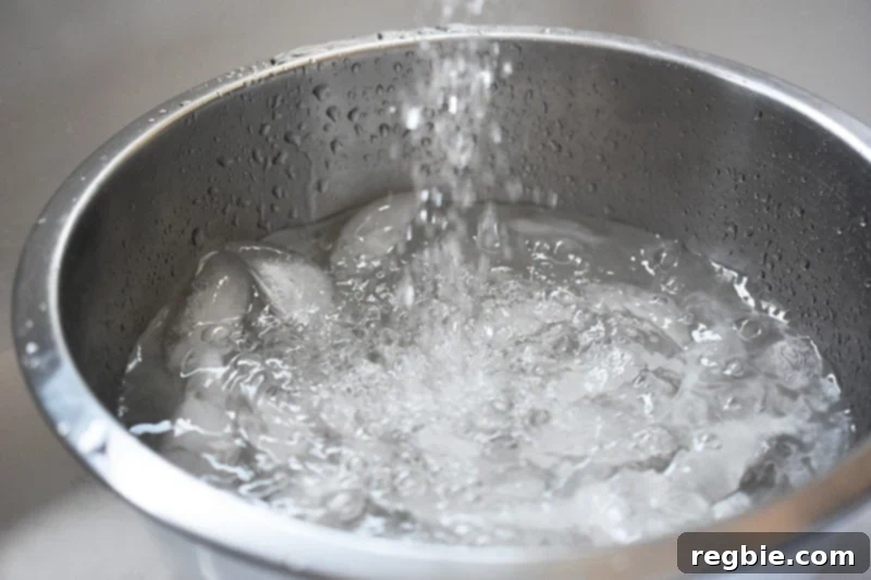 A metal bowl being filled with ice and water, preparing for the ice bath for daikon noodles.