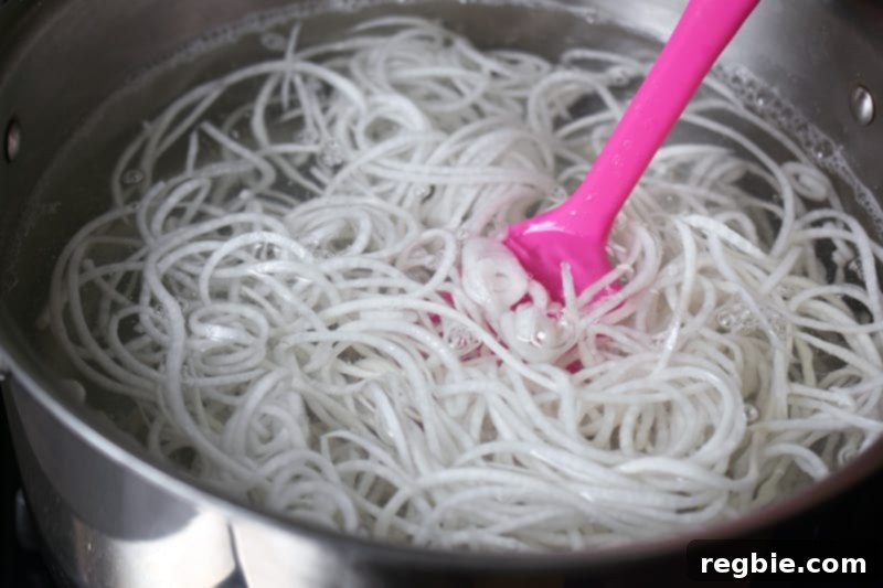 Daikon noodles gently cooking in a pot of boiling water, stirred with a pink spatula.
