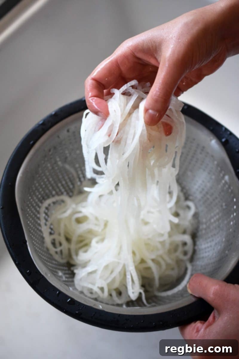 Someone lifting the thoroughly chilled daikon noodles from the colander, ensuring they are well-drained.