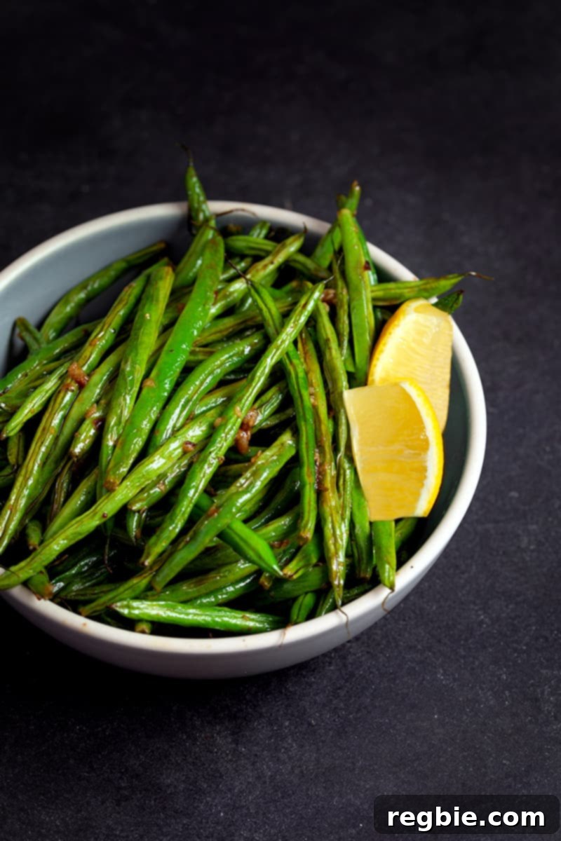 Crisp Lemon-Garlic Roasted Green Beans 11 A bowl filled with roasted green beans with lemon and garlic and two lemon slices.