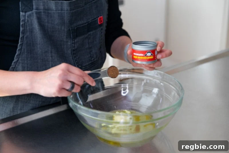 Crisp Lemon-Garlic Roasted Green Beans 4 Measuring the marinade ingredients for roasted green beans with lemon and garlic into a large glass mixing bowl. A woman is adding a spoonful of Nom Nom Paleo's Magic Mushroom Powder to the bowl.