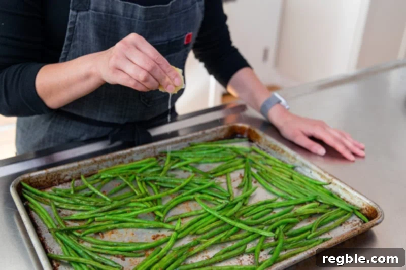 Crisp Lemon-Garlic Roasted Green Beans 10 Squeezing a lemon wedge onto a pan of roasted green beans with garlic.