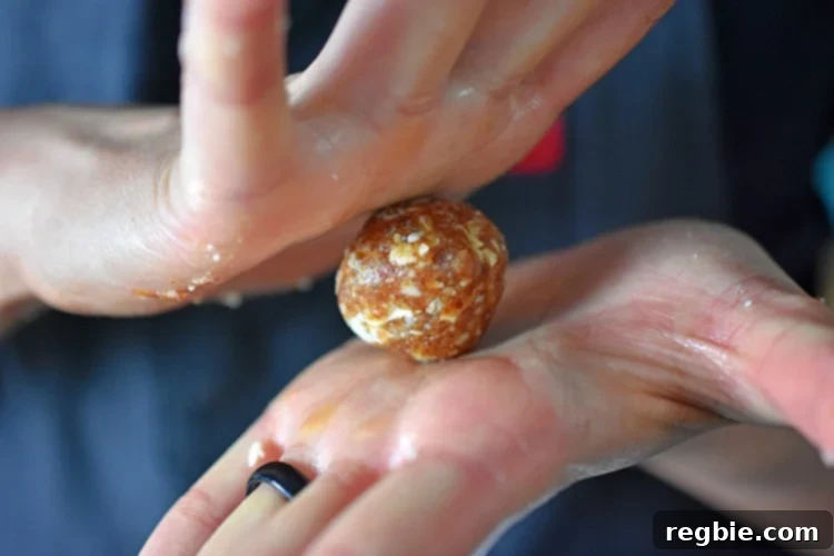 A detailed close-up shot of hands skillfully rolling a portion of the paleo energy ball mixture into a perfectly spherical shape, illustrating the final manual step before the coating process.