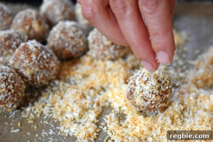 Vegan energy balls being generously coated in a soft, fluffy pile of toasted shredded coconut, creating an attractive and delicious outer layer that enhances both flavor and texture.
