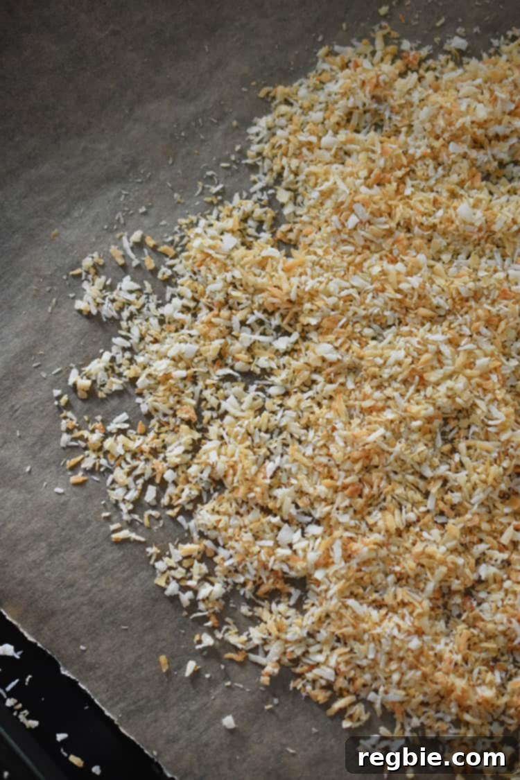 Perfectly toasted shredded coconut, a vibrant golden brown, evenly scattered across a parchment-lined baking sheet, emitting a delightful aroma.
