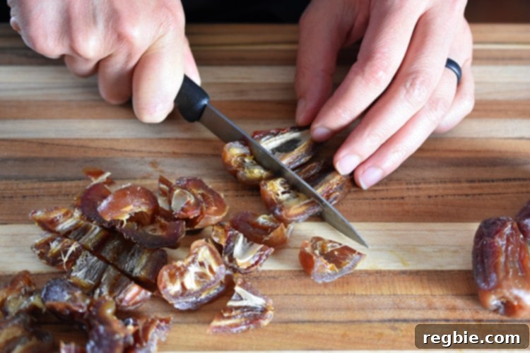 An individual expertly chopping a generous pile of pitted Medjool dates on a clean wooden cutting board, meticulously preparing them for incorporation into the energy ball mixture.