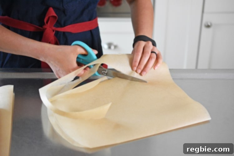 Someone carefully cutting a half-heart shape on folded parchment paper with kitchen shears.