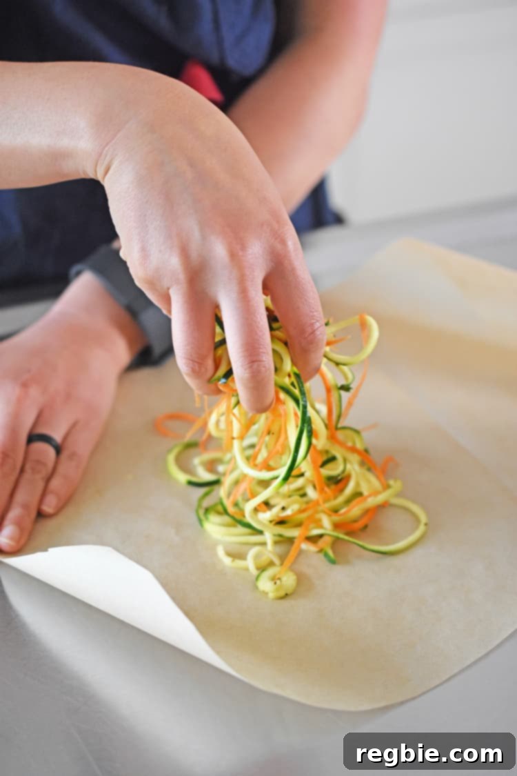 Adding seasoned spiraled carrots and zucchini onto one side of a heart-shaped parchment paper.