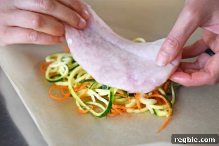 Placing a piece of white fish fillet on top of the spiraled vegetables inside a parchment paper heart.
