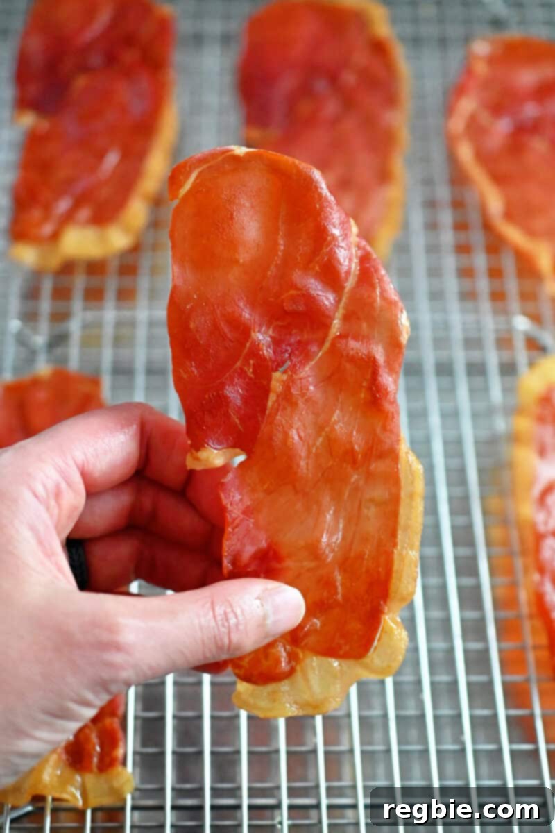 Golden Prosciutto Snaps 3 A hand is holding a crispy prosciutto chip that was picked up from a metal cooling rack