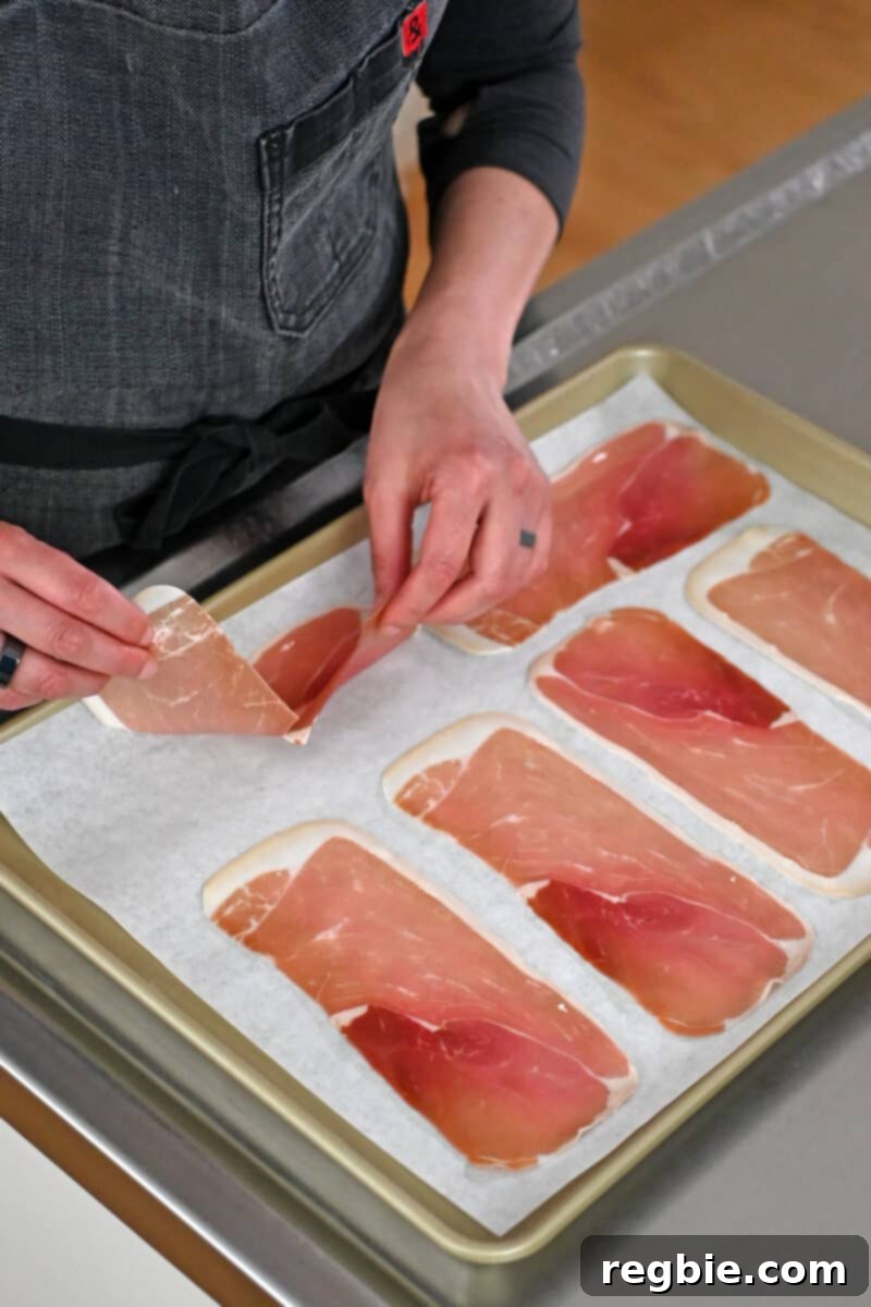 Golden Prosciutto Snaps 5 Two hands are placing thinly sliced prosciutto slices on a parchment-lined rimmed baking sheet to make crispy prosciutto